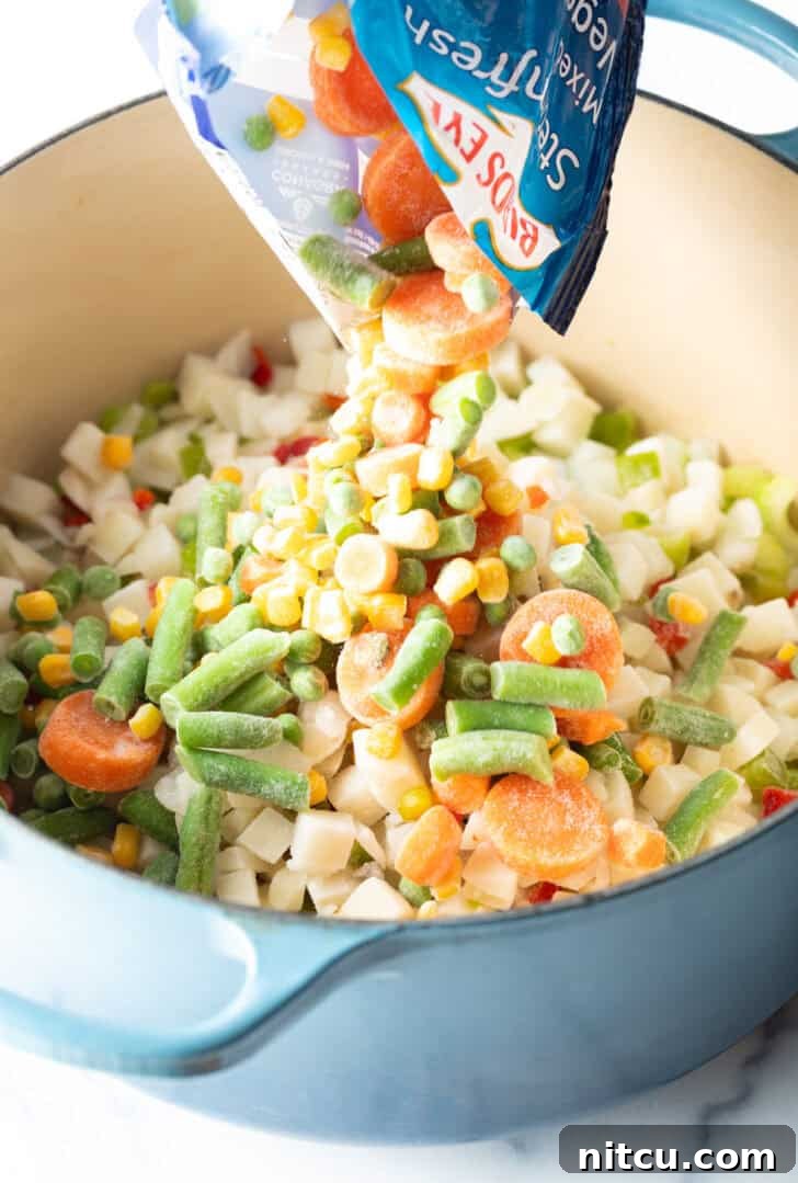 Pouring a mix of frozen corn, green beans, carrots, and peas into a large cooking pot.