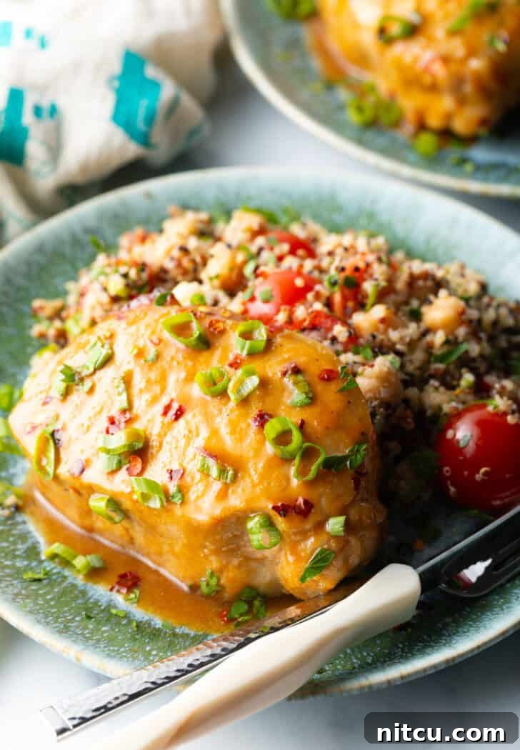 A perfectly baked pork chop, richly coated in a glistening savory-sweet glaze and garnished with fresh chopped scallions, presented on a white plate alongside a vibrant quinoa salad with cherry tomatoes.