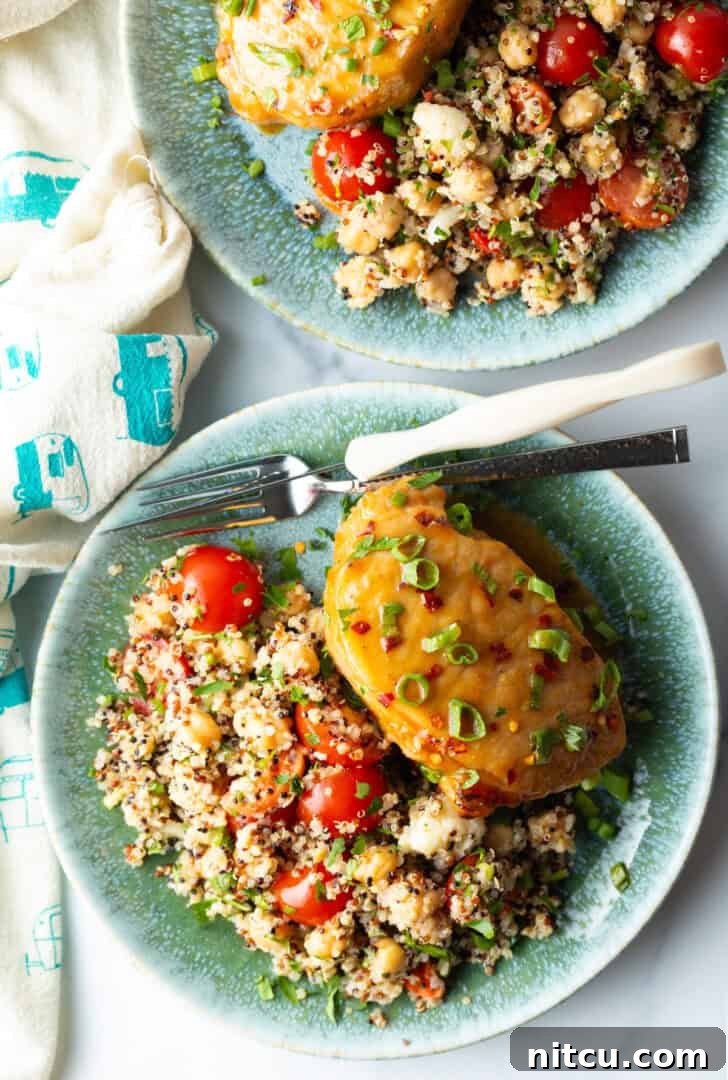A perfectly cooked baked pork chop, gleaming with its savory-sweet glaze and adorned with fresh chopped scallions, elegantly plated beside a wholesome quinoa salad featuring vibrant tomatoes.