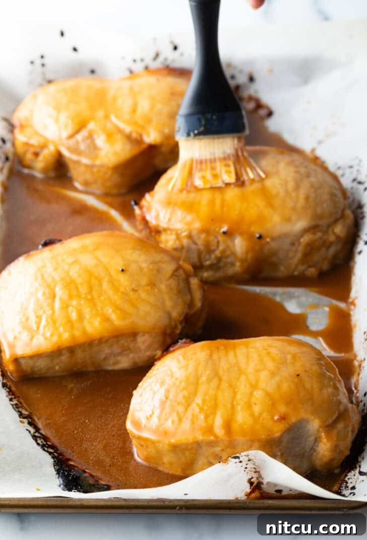A close-up perspective of a brush generously coating boneless pork chops with the homemade glaze, illustrating the even distribution of flavor-packed sauce.
