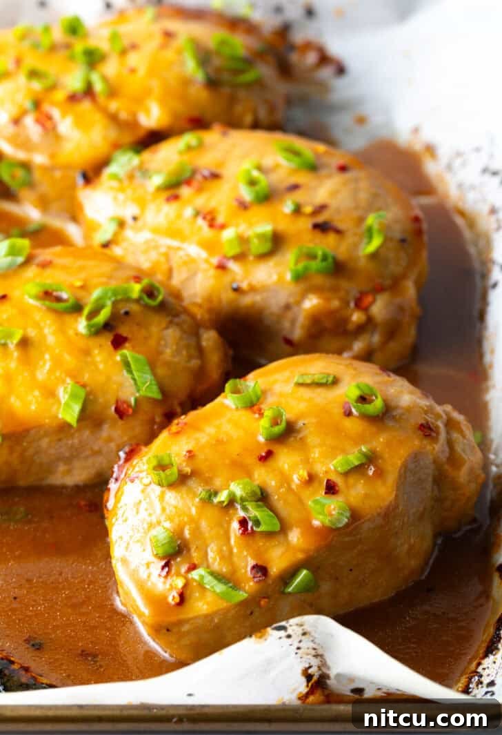 Beautifully glazed pork chops, freshly baked and generously covered with bright green onions, resting on a baking sheet, emanating a delicious aroma and ready for serving.