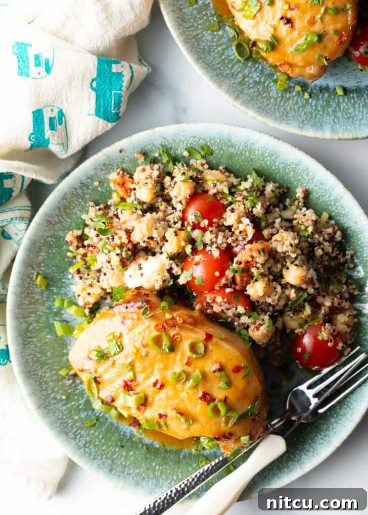 A perfectly baked pork chop, covered with a shiny glaze and fresh scallions, elegantly plated beside a wholesome quinoa salad with bright red tomatoes, presenting a complete and inviting meal.