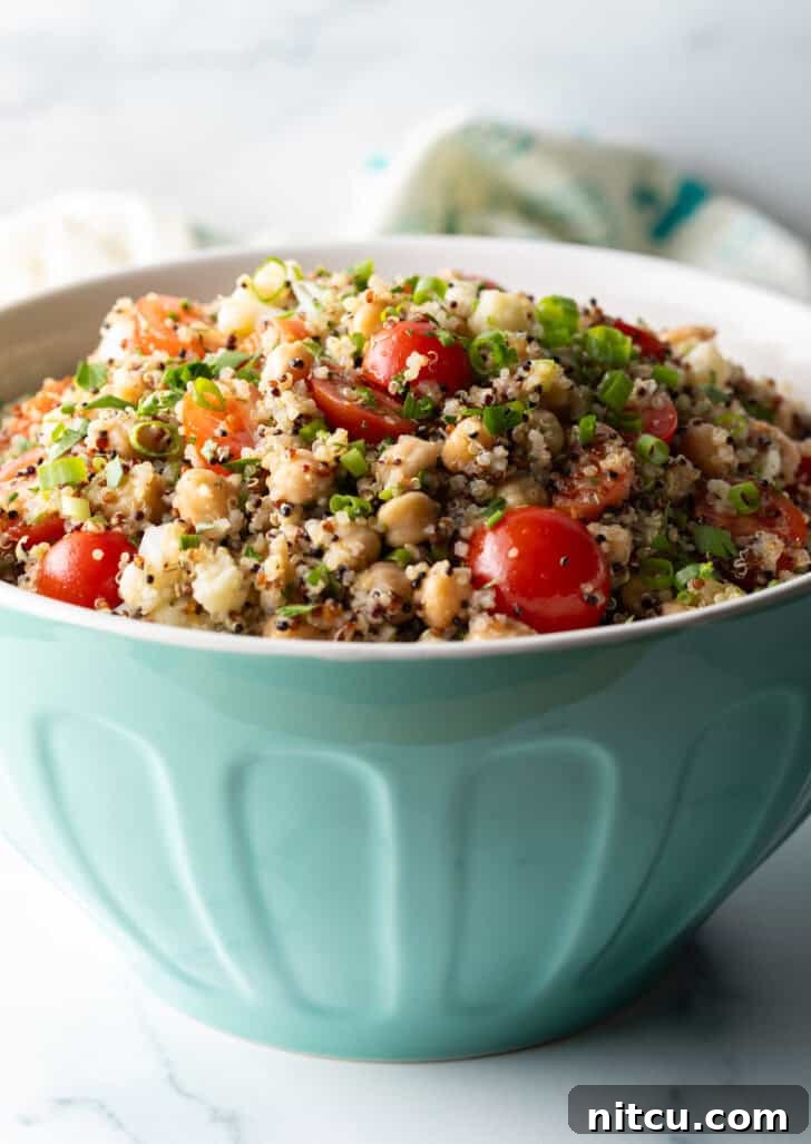 Bowl of quinoa salad with cherry tomatoes, chopped fresh herbs, and chickpeas.