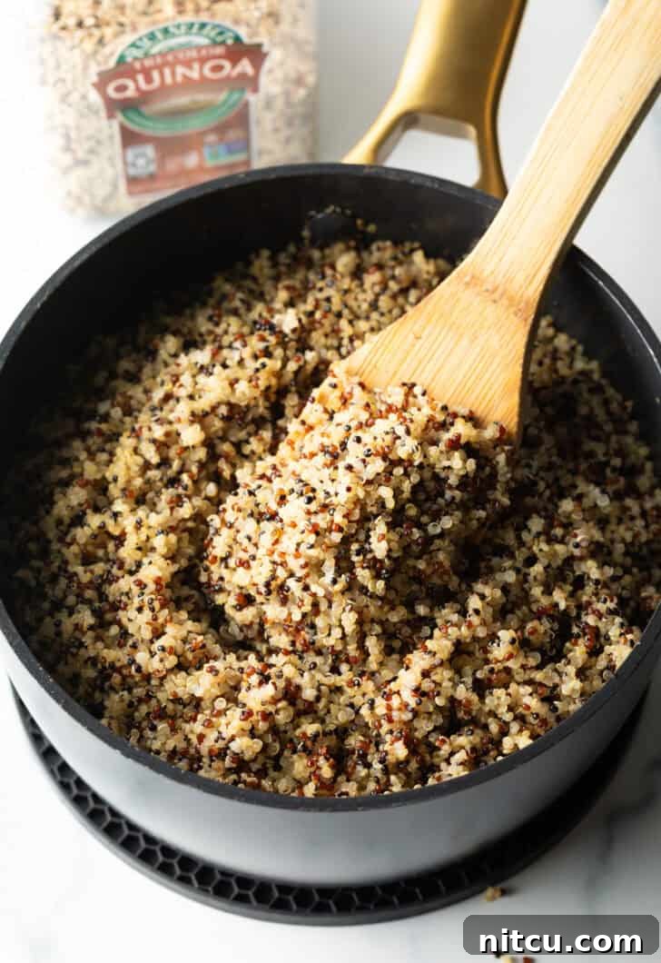 Stirring fluffy quinoa in a large black skillet with a wood spatula.