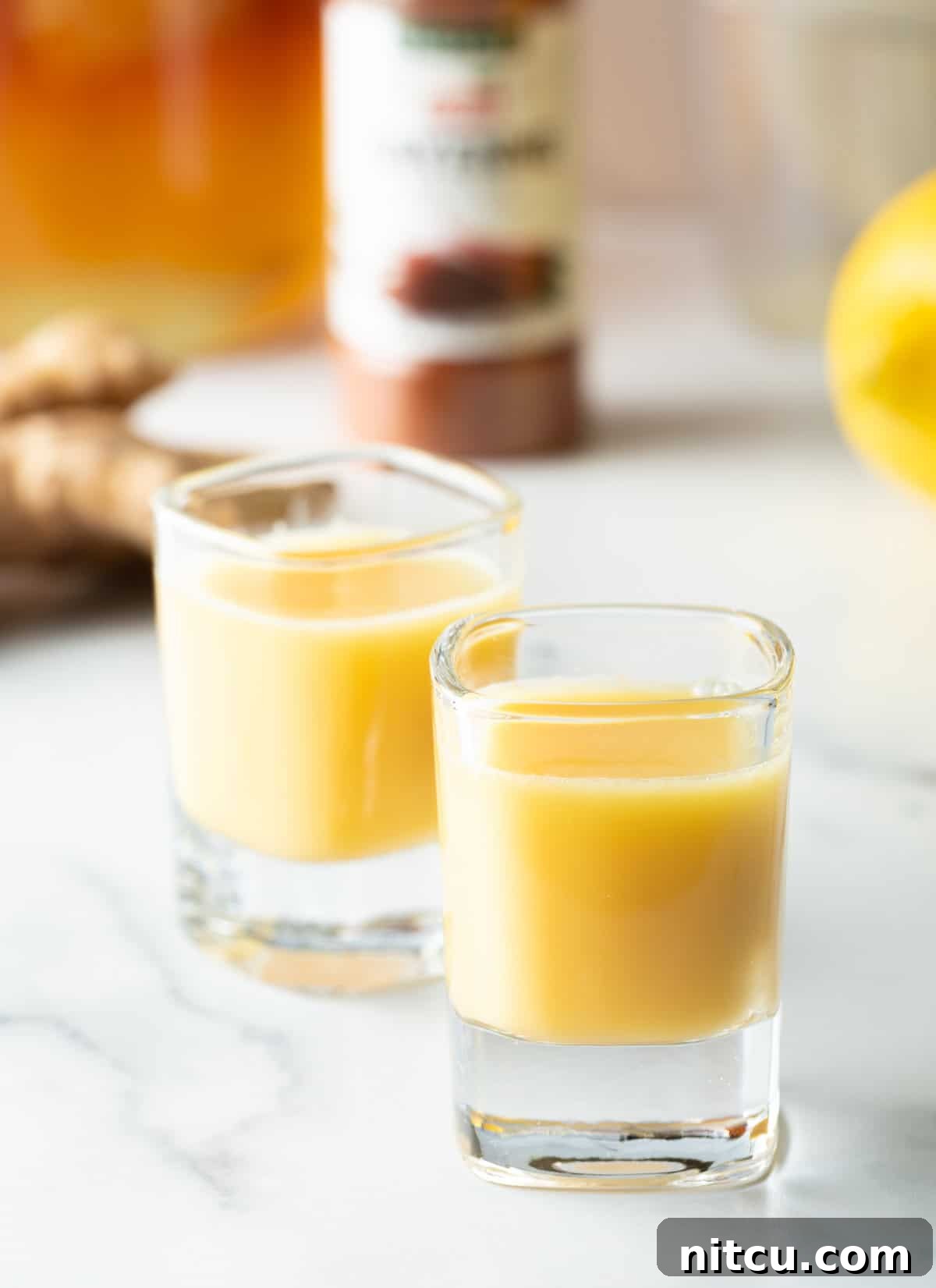 Two shot glasses filled with vibrant yellow ginger shot liquid, ready to be consumed.