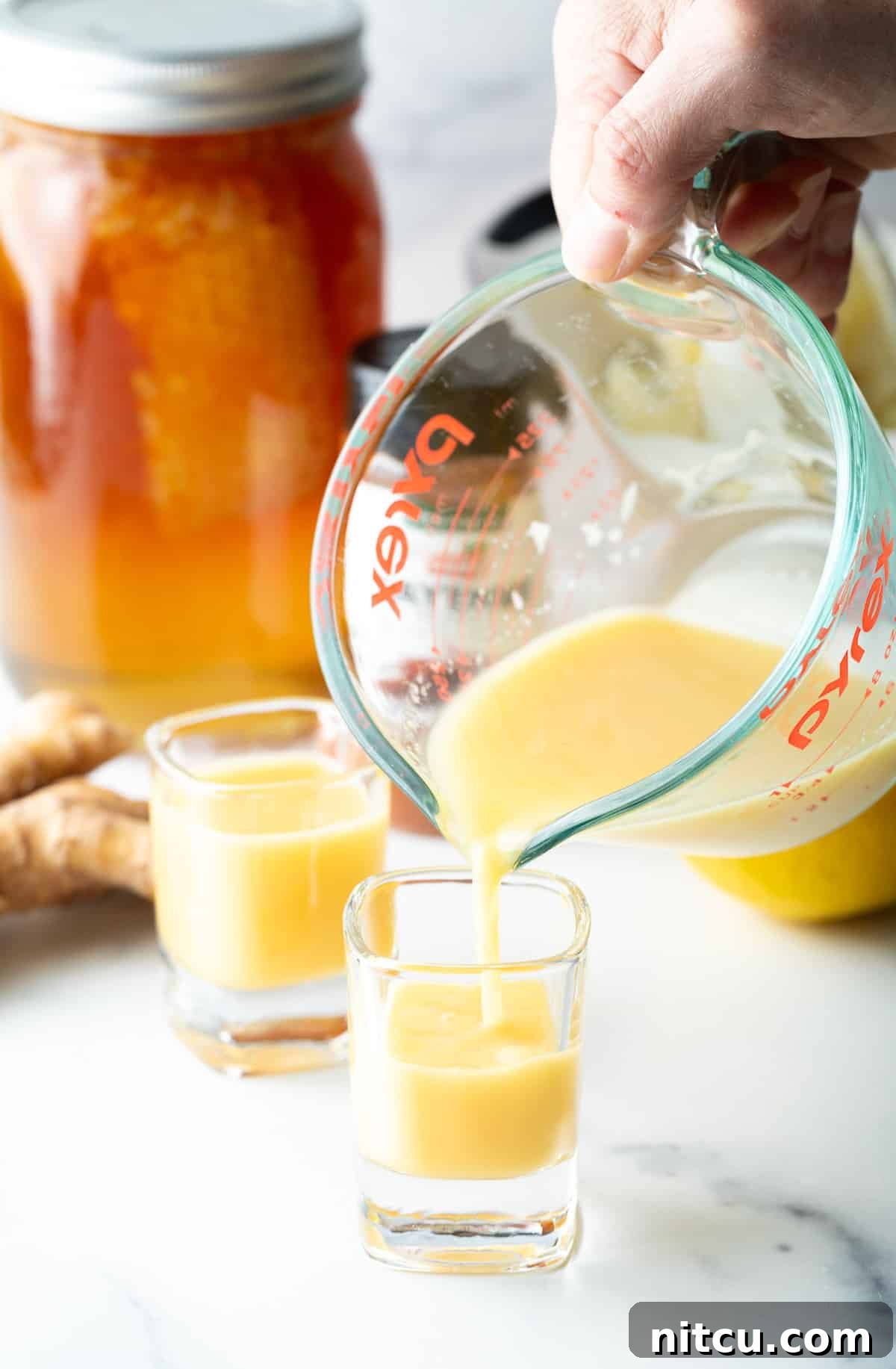 Pouring vibrant yellow liquid from a glass measuring pitcher into two shot glasses, ready for consumption.