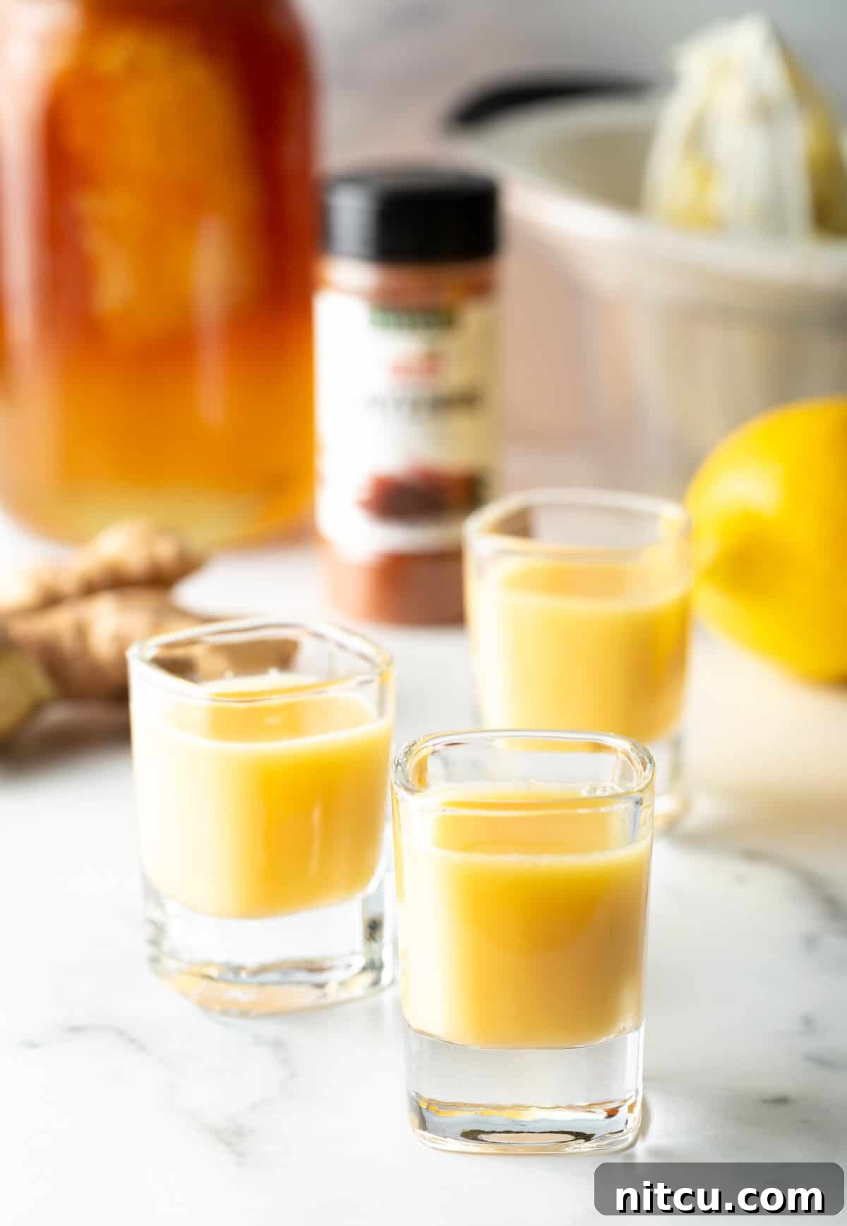Three shot glasses with golden yellow ginger shots, garnished with lemon slices, ready for serving.