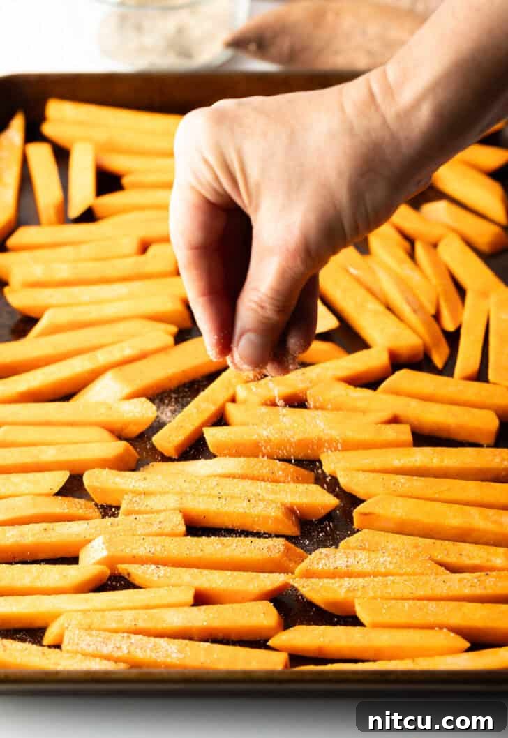 Hand placing raw slices of potatoes on a baking sheet.