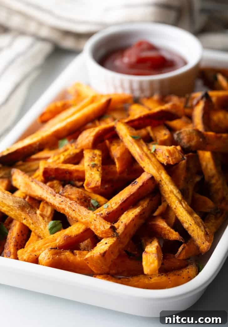 Piles of cooked baked or air fryer sweet potatoes on a large serving pan with a white ramekin of ketchup.
