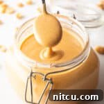 A spoon taking a scoop of peanut butter from a glass jar, showing the butter to camera.