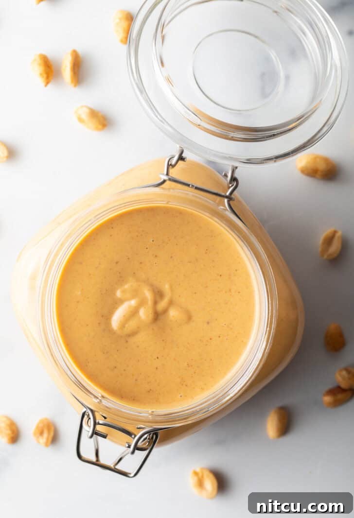 Top down view of a glass container filled with freshly made, golden-brown homemade peanut butter, ready for storage.