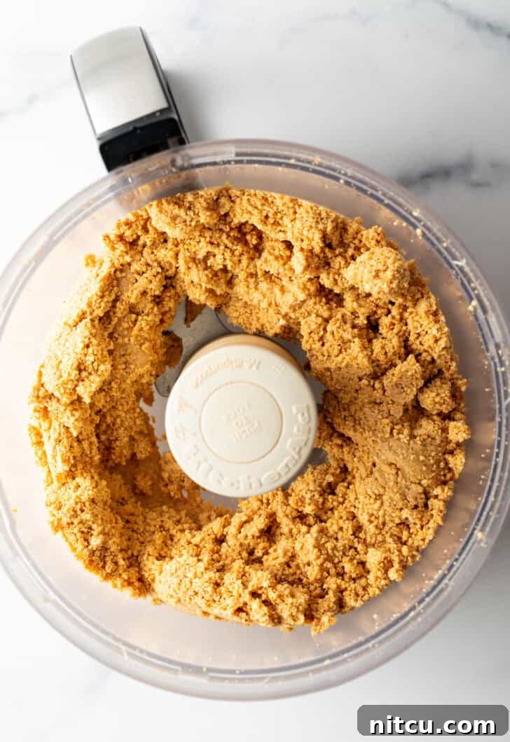Peanuts blending further, reaching a coarse crumb stage in the food processor.