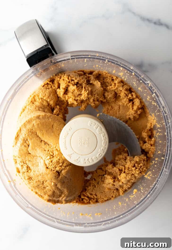 The peanuts have formed a thick, dough-like paste in the food processor, signaling progress.