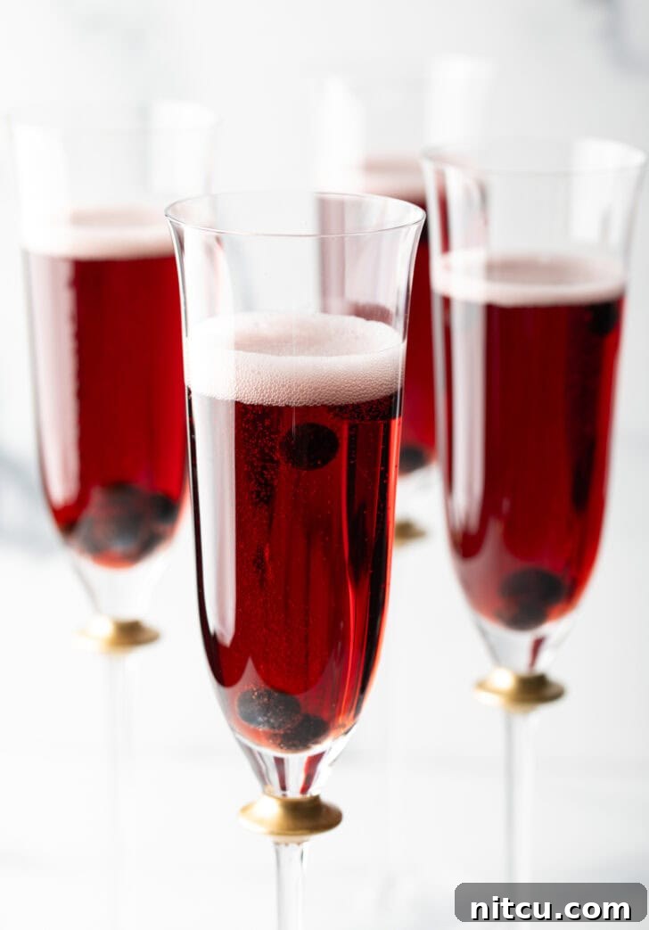 Four fluted glasses with deep red Kir Royale cocktail drinks, elegantly presented for a celebration.