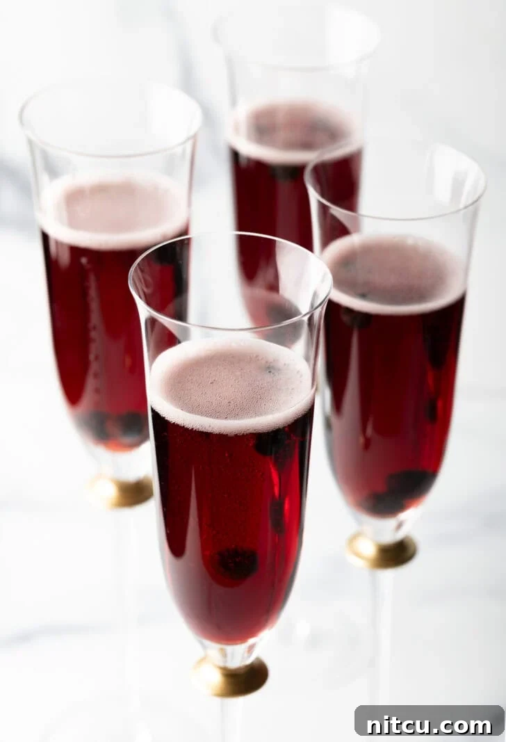 Another perspective of four fluted glasses filled with rich red Kir Royale cocktails.