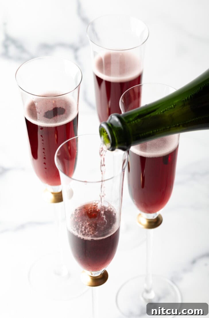 Chilled champagne being poured over the crème de cassis in a fluted glass.