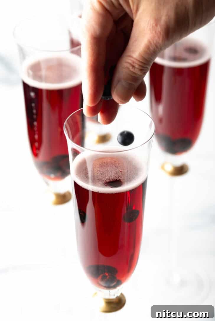 A hand delicately sprinkling dried blackcurrants into a Kir Royale cocktail.