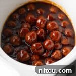 White slow cooker filled with meatballs in bbq sauce.
