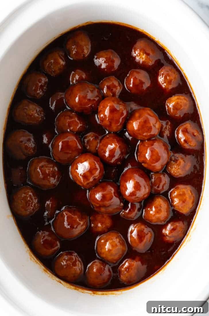 White slow cooker filled with meatballs in bbq sauce.