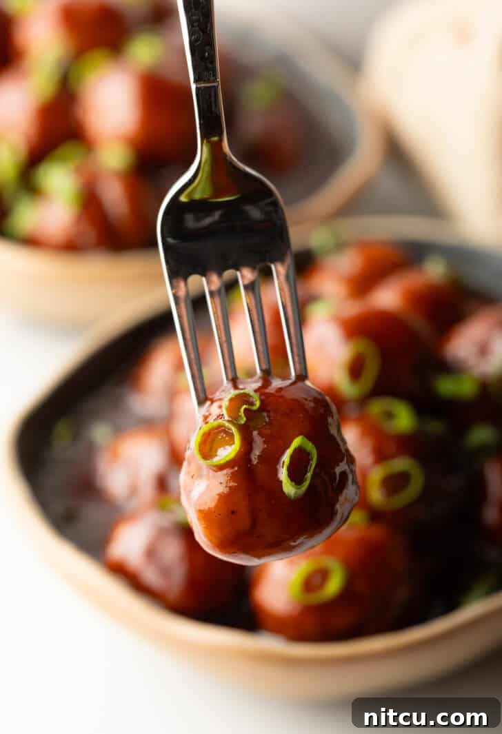 A fork is holding a bbq sauce-coated meatball to camera.