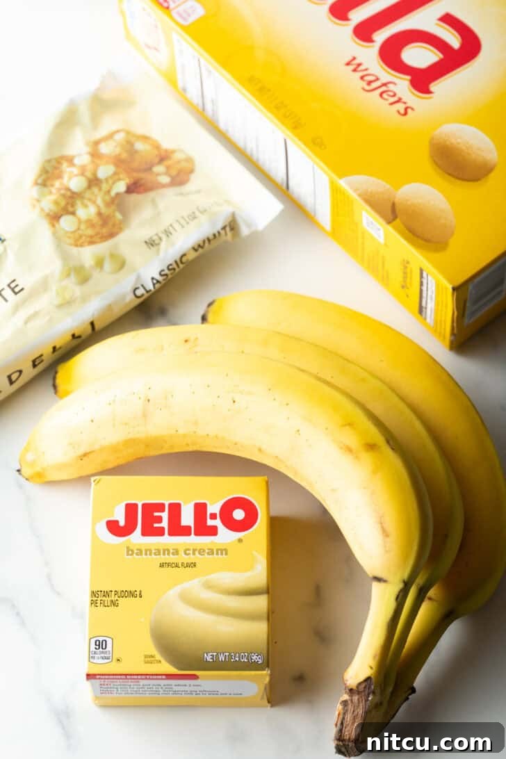 Recipe ingredients: bunch of 3 bananas, package of Jell-o instant banana pudding, bag white chocolate chips, and box of Nilla wafters, laid out for baking.