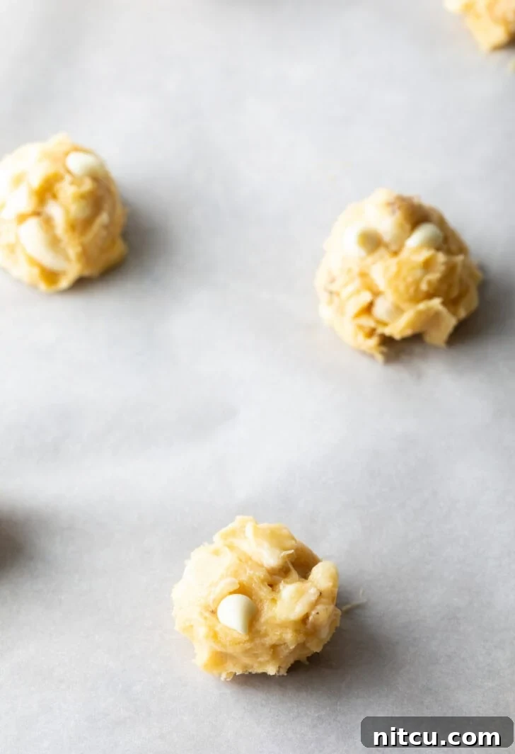 Several balls of cookie dough placed on a baking sheet with parchment paper, spaced for baking.