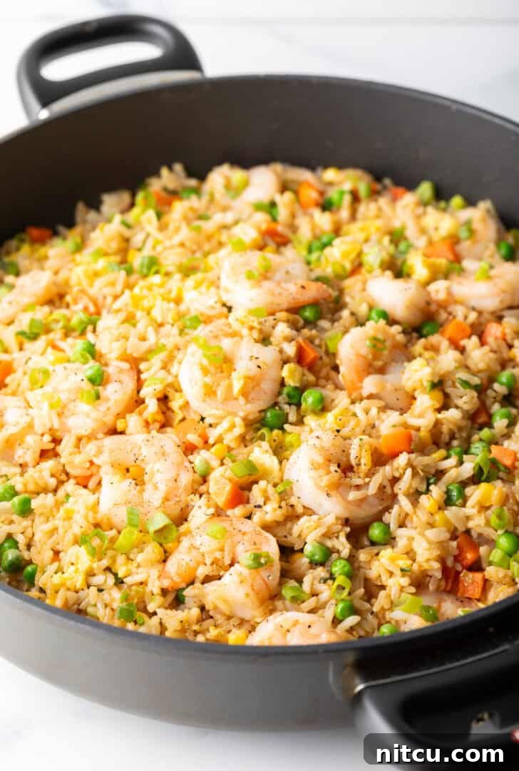 Deep black skillet with cooked shrimp, rice, scrambled eggs, and veggies, ready to be served.
