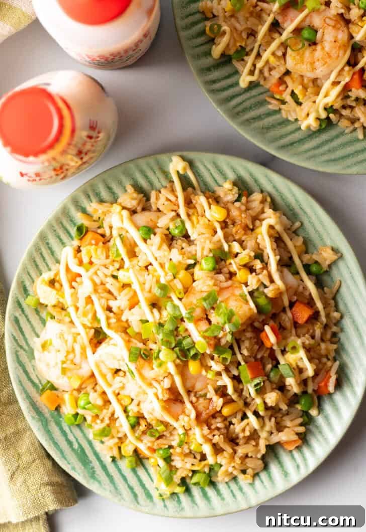 Top down view of a green plate piled with shrimp fried rice, topped with a zig zag drizzle of yum yum sauce, ready to be enjoyed.