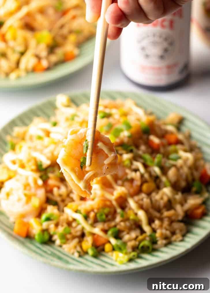 Close-up shot of chopsticks holding a perfectly cooked shrimp against a blurred background, highlighting its succulent texture.