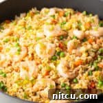Deep black skillet with cooked shrimp, rice, scrambled eggs, and veggies.