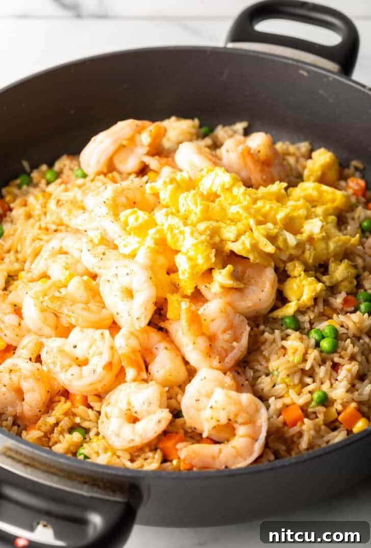 A deep black skillet brimming with a delicious medley of cooked shrimp, rice, fluffy scrambled eggs, and colorful vegetables, perfectly stir-fried.
