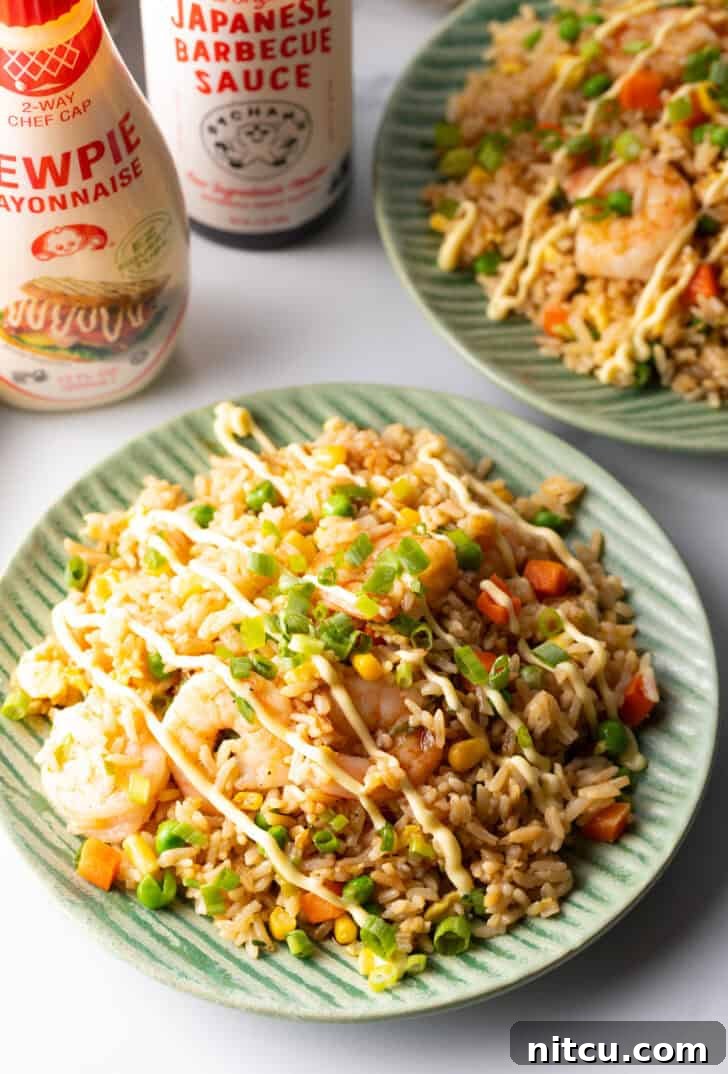 A close-up shot of a green plate generously piled with shrimp fried rice, topped with a beautiful zig-zag drizzle of creamy yum yum sauce.