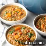 Three white bowls of lentil soup with carrots and kale.