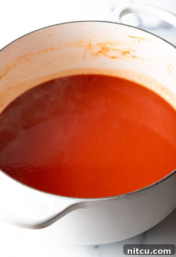 Bright red tomato sauce being poured into a pristine white cooking pot, ready for simmering.