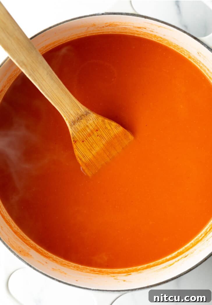 A top-down view of a large pot brimming with rich, creamy tomato soup, a wooden spatula resting invitingly within its depths.