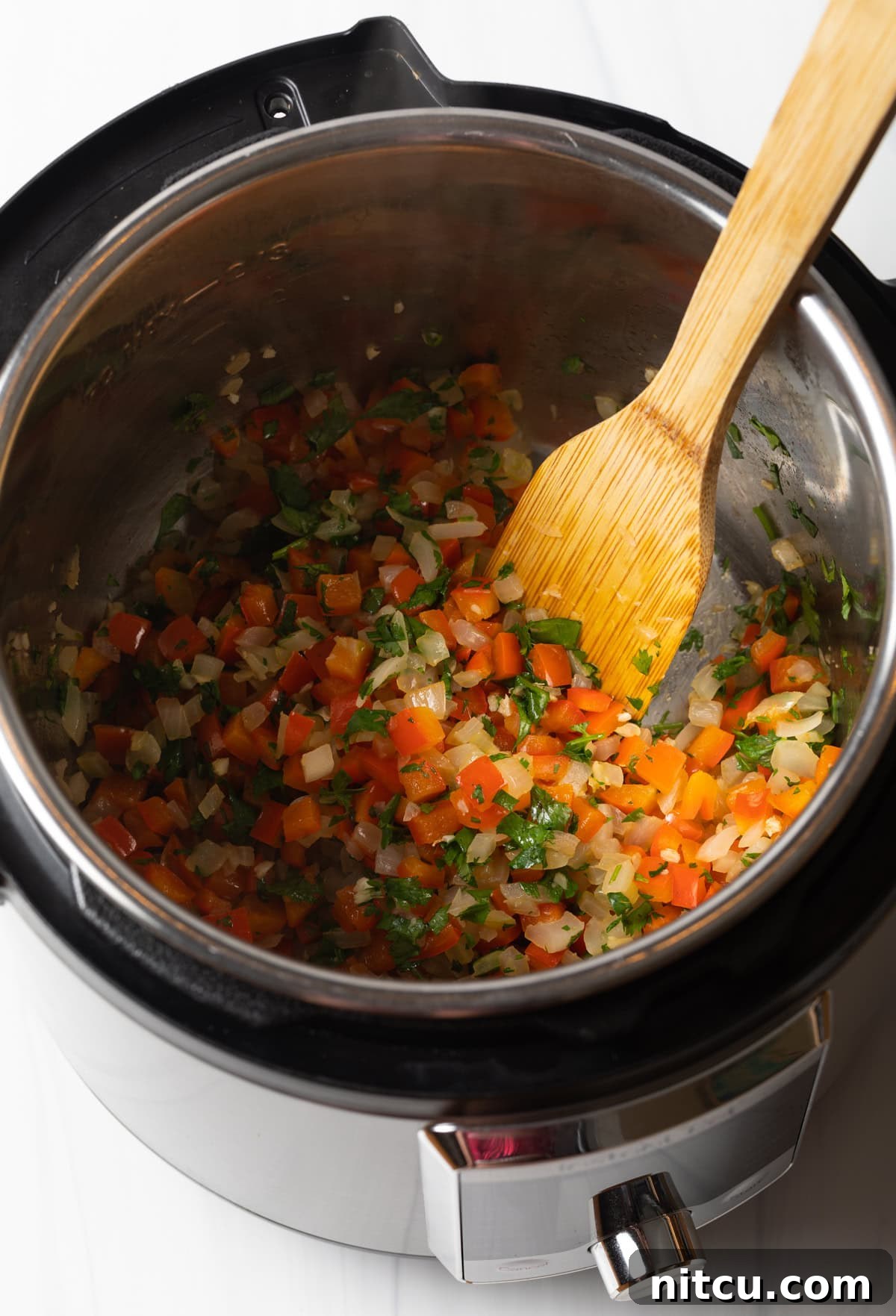Sauteed red peppers and onions in an instant pot with a wooden spatula.