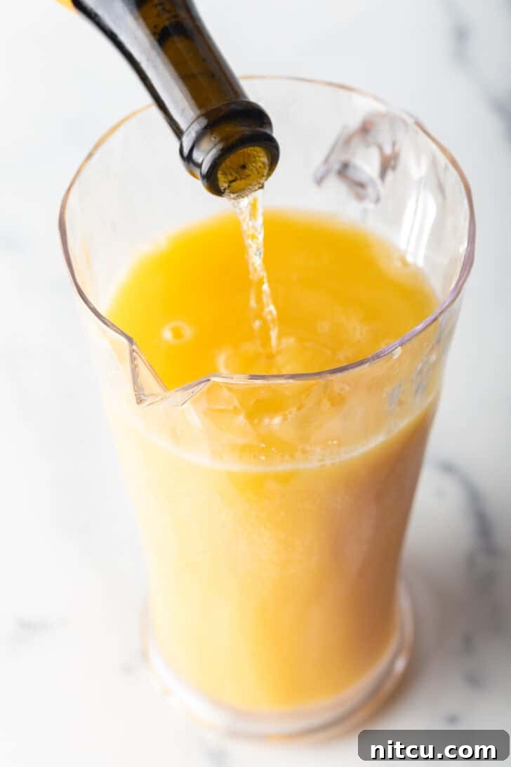 Pouring sparkling wine form the bottle into a glass pitcher with orange juice.