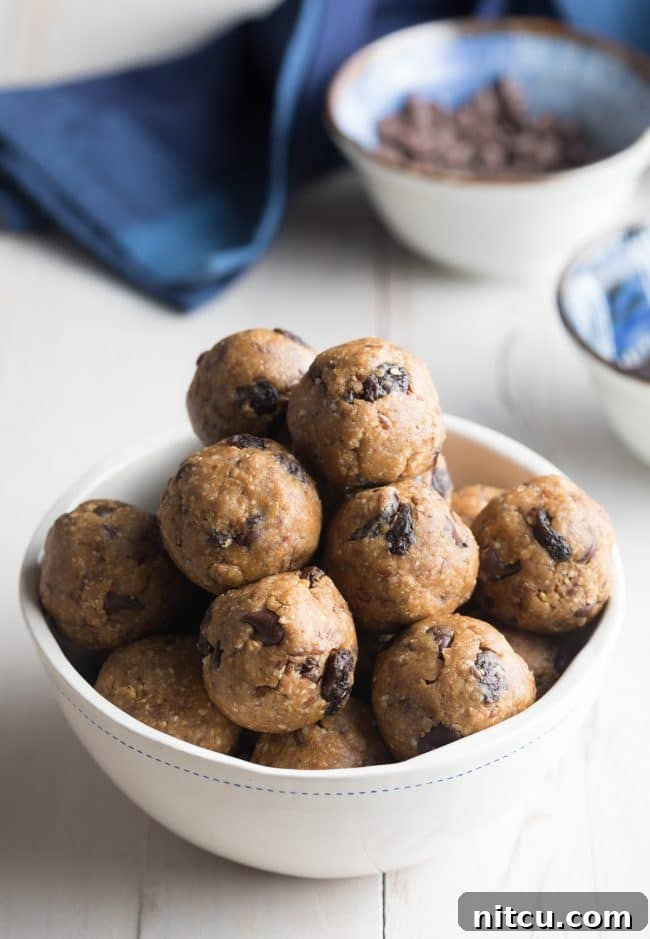 White bowl brimming with oatmeal energy balls that are speckled with peanut butter chocolate chips and raisins. A healthy and delicious snack.