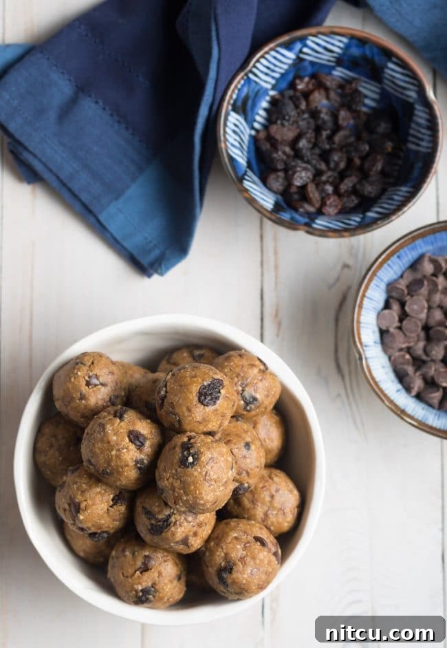 Top down view of a white bowl brimming with oatmeal energy balls that are speckled with peanut butter, chocolate chips and raisins, showcasing their texture and ingredients.
