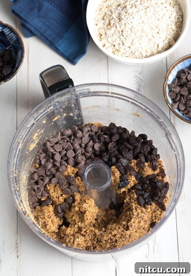 Adding chocolate chips to the food processor with no bake oatmeal cookie dough, ensuring an even distribution of sweetness.