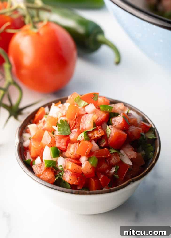 A white bowl of fresh pico de gallo with chopped tomatoes, onion, jalapeno, and cilantro.