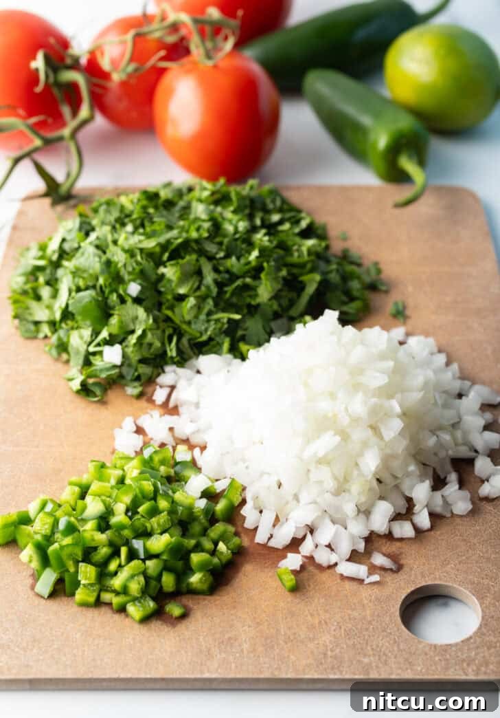Recipe ingredients in separate piles on a cutting board: Fresh chopped cilantro, jalapenos, and onion.