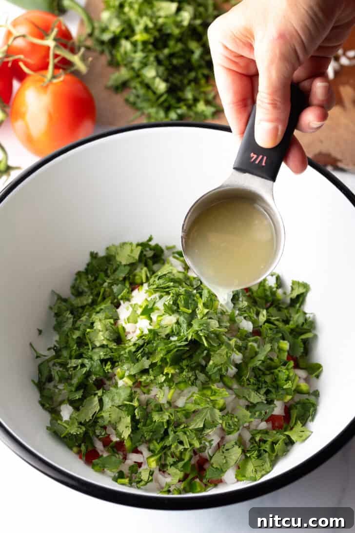 Fresh chopped cilantro has been added to the bowl. A hand is pouring lime juice from a small metal measuring cup.