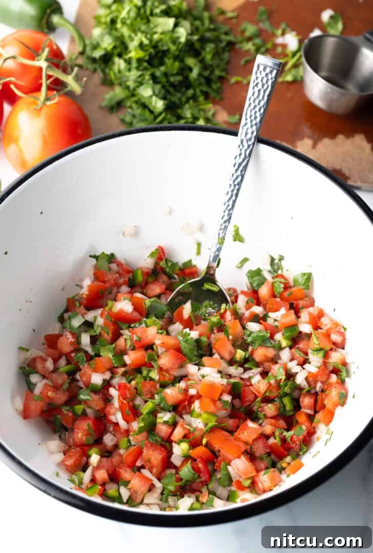 Combining the pico do gallo ingredients in a white mixing bowl with a spoon.