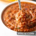 A metal spoon is showing a scoop of roasted salsa scooped from a white bowl.
