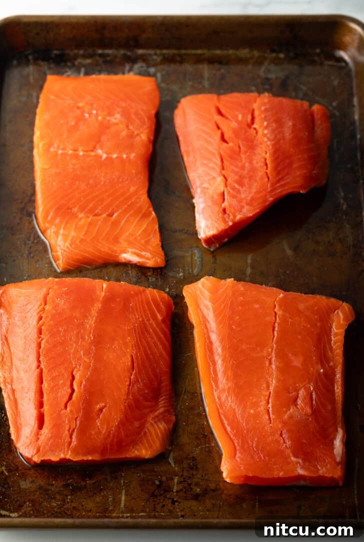 4 raw pieces of salmon filets on a baking sheet.