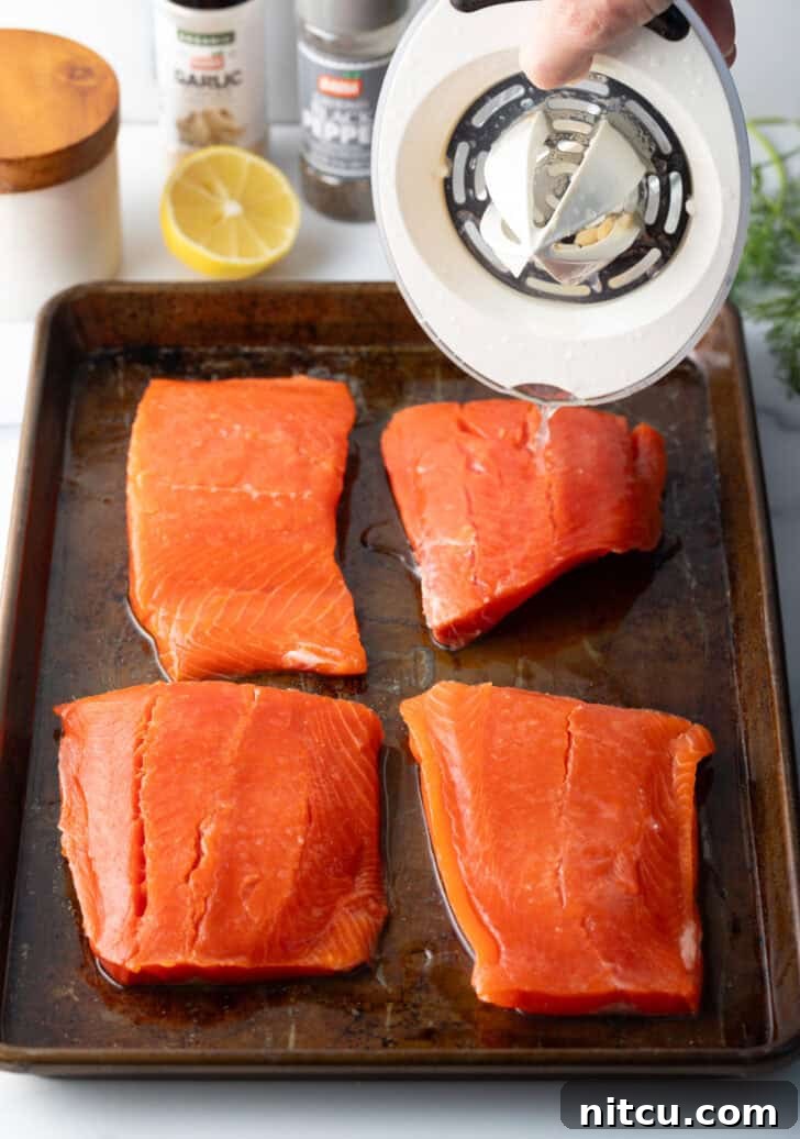 Raw salmon filets on a baking sheet, seasoned and ready for the oven.