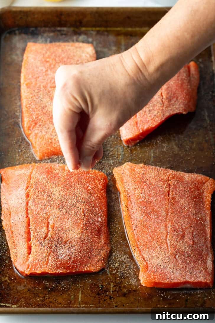Close-up of raw salmon seasoned with spices on a baking sheet.
