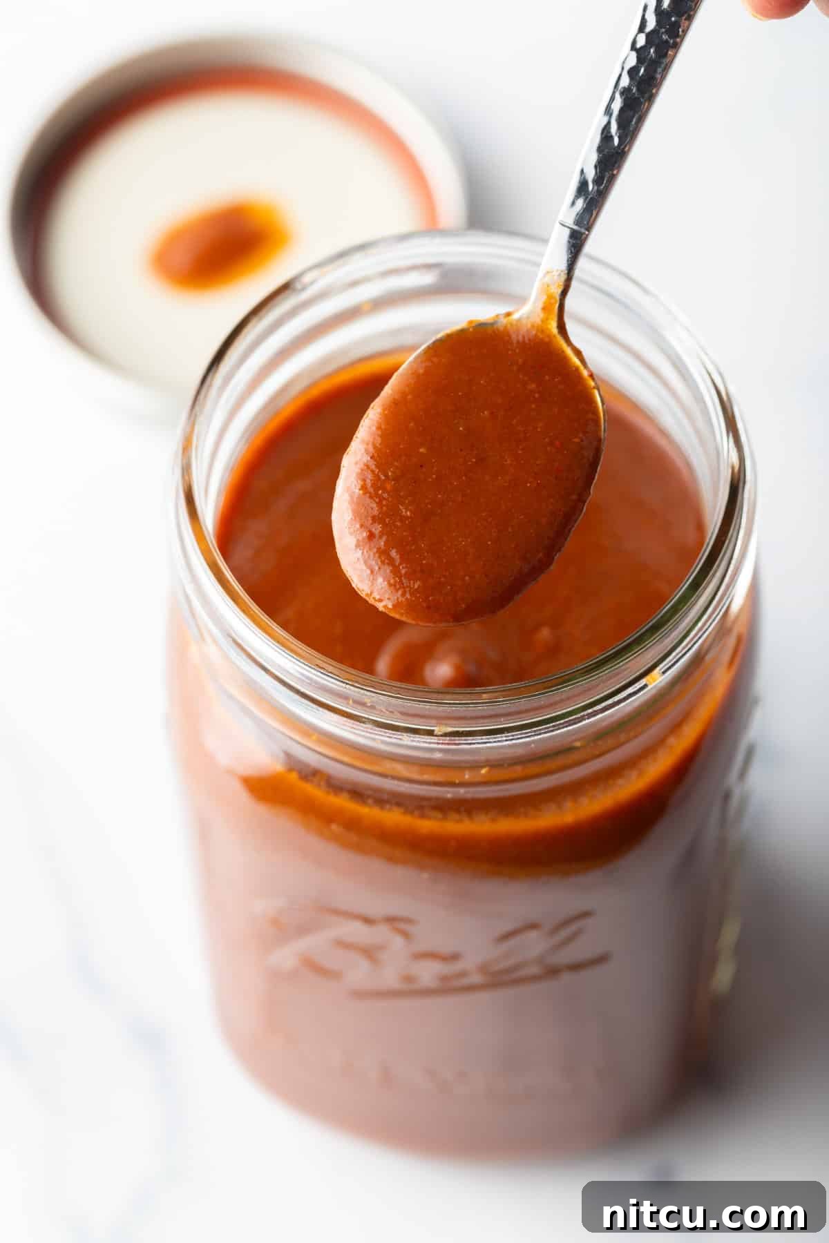 Spoonful of red enchilada sauce being held to camera over a large jar.