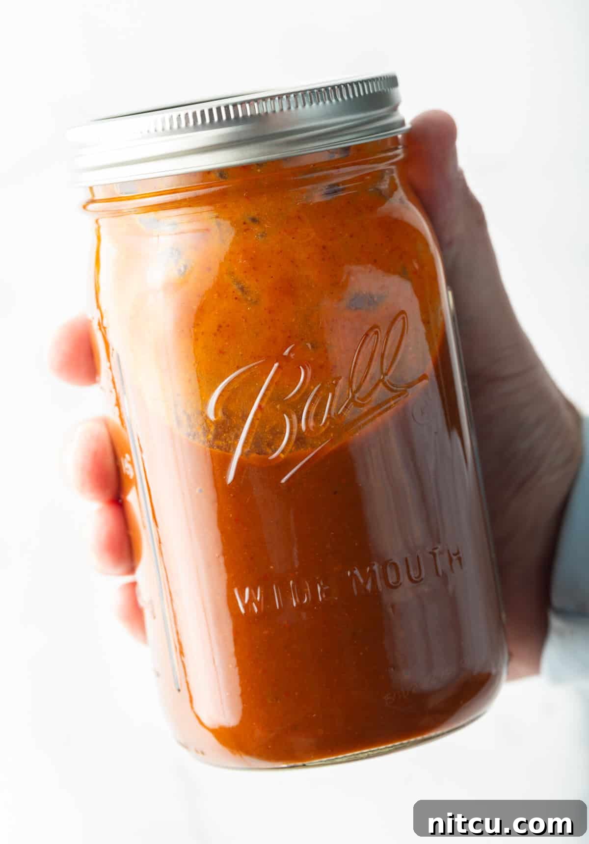 Hand holding a large glass mason jar filled with red enchilada sauce.